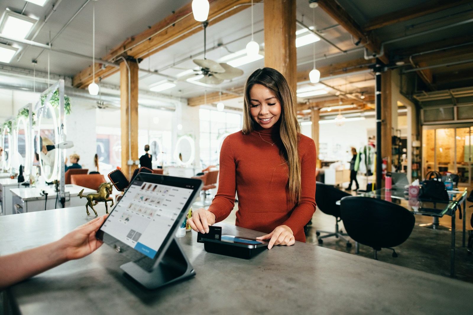 A woman in a rust-colored sweater paying with a card at a salon counter